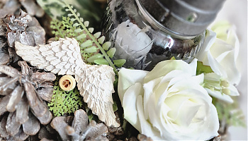 Toboz sírdísz - Festett toboz koszorú, mécsessel, krémfehér virágokkal, angyalszárnnyal. A termék 22cm átmérőjű. 